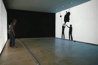 Photo: two people stand in a gallery facing a whit...