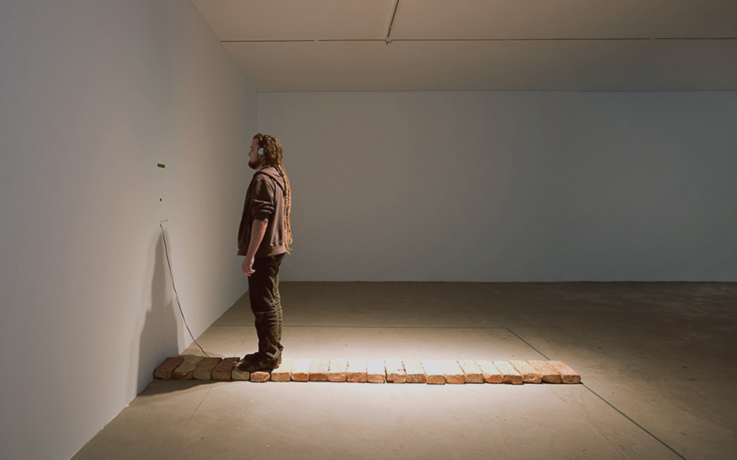 Installation photo. Man in a gallery stands on a r...