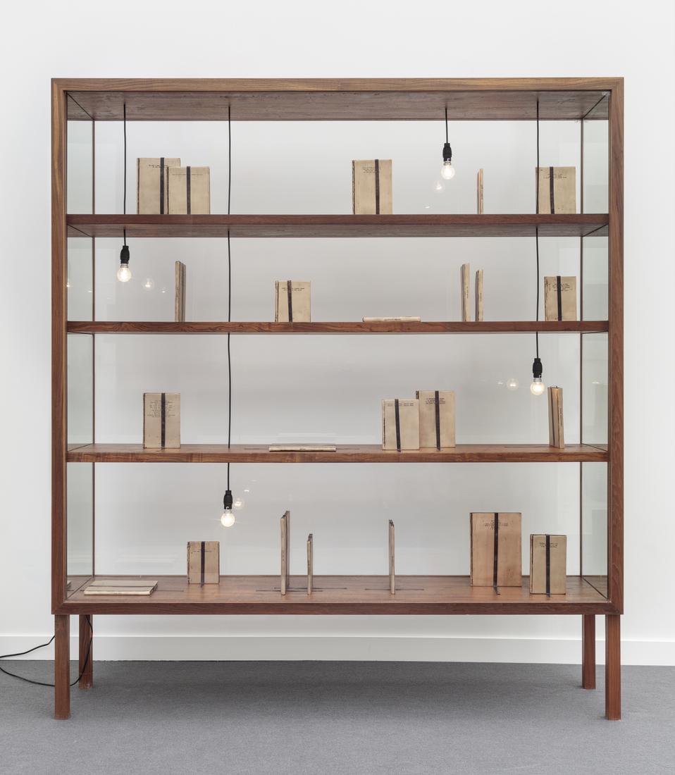 Glass vitrine with wooden shelfs displays beige bo...