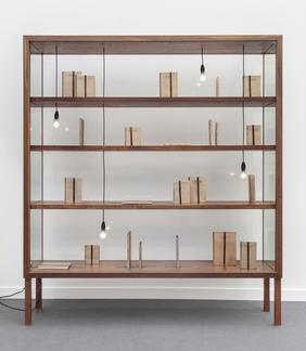Glass vitrine with wooden shelfs displays beige bo...